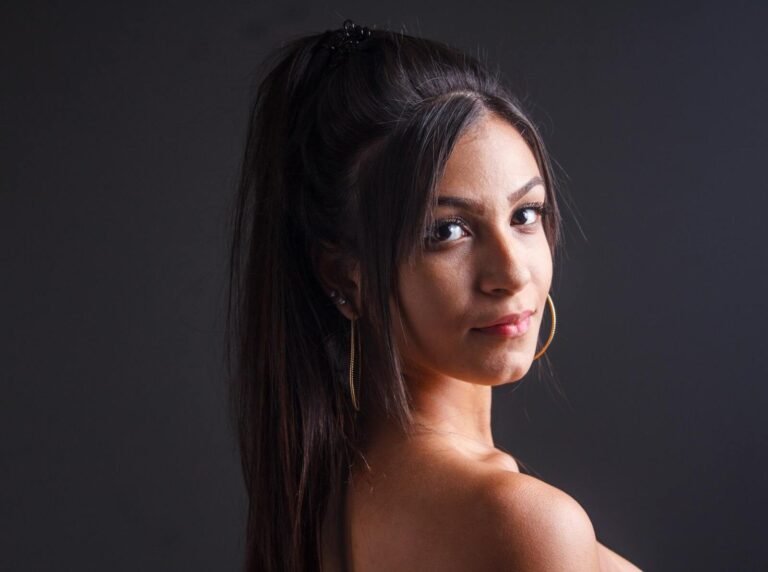Elegant studio portrait of a woman with long dark hair and hoop earrings, facing sideways.