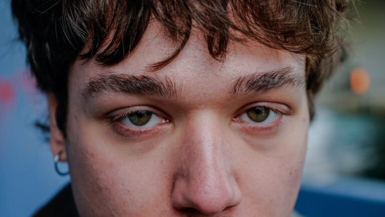 A detailed close-up portrait showcasing the youthful features of a young adult with striking green eyes.