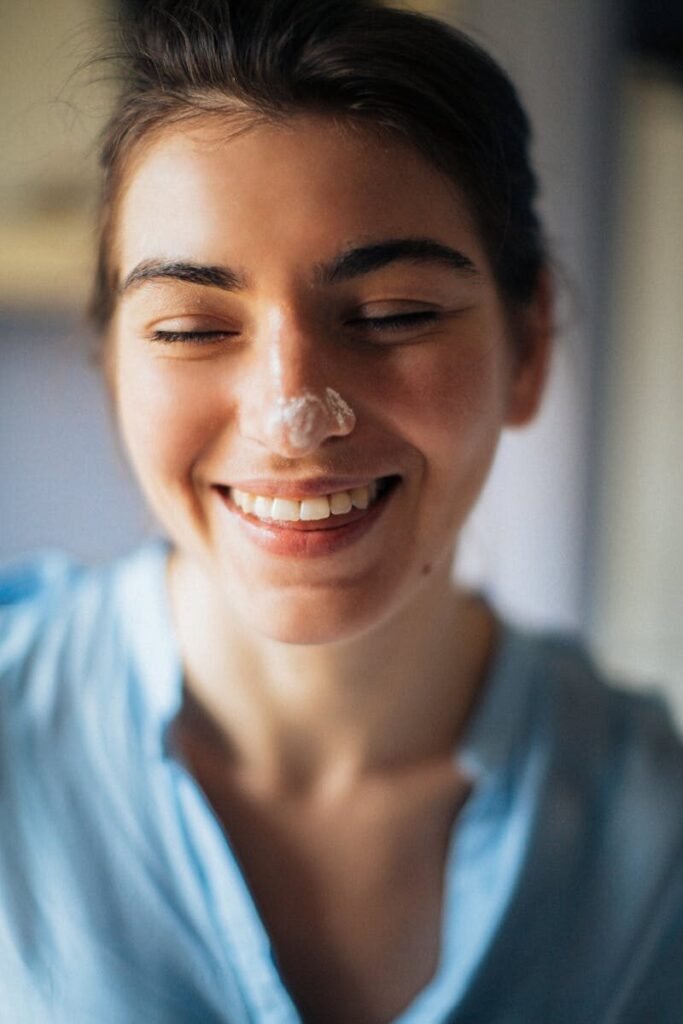 Close-up portrait of a smiling woman with cream on her nose.