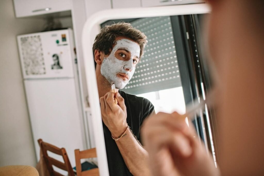 A man applying a face mask while looking into a mirror, emphasizing self-care and grooming.