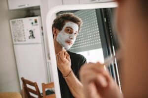 A man applying a face mask while looking into a mirror, emphasizing self-care and grooming.