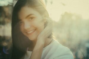 A beautiful woman smiles warmly while outdoors in soft sunlight.