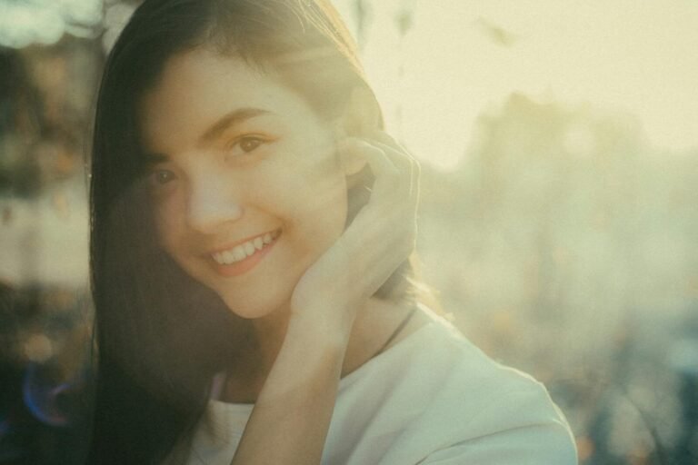 A beautiful woman smiles warmly while outdoors in soft sunlight.