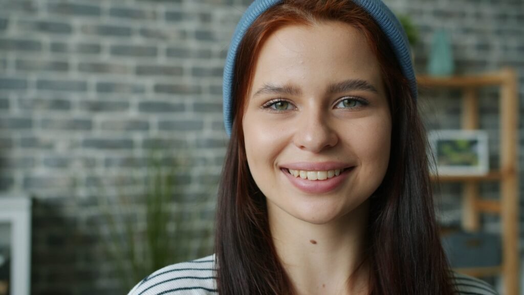 Young woman with red hair wearing a blue headband smiling.