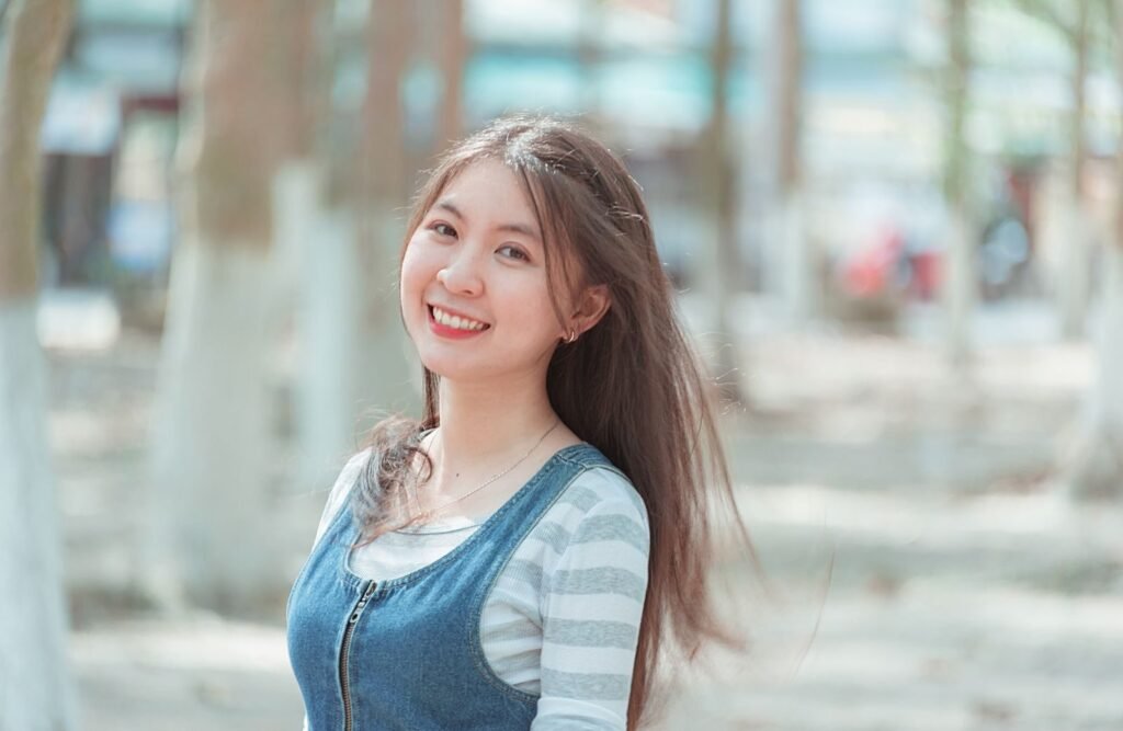 A cheerful young woman smiling outdoors in a casual attire, captured on a sunny day.