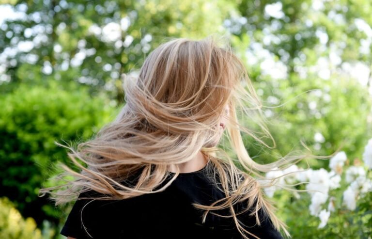Blonde woman outside with hair blowing in the wind on a sunny summer day.
