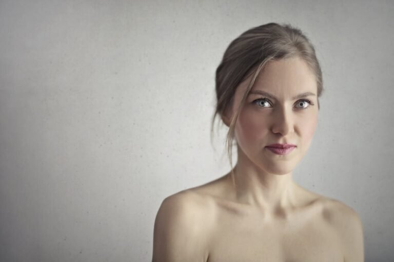 Stunning close-up portrait of a young woman with captivating eyes and a serene expression against a gray background.