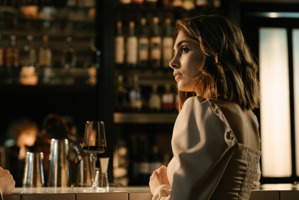 A woman in an elegant dress sitting at a bar, enjoying a glass of wine, creating a warm and intimate atmosphere.