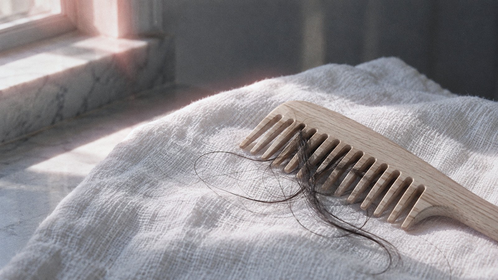 Wooden wide-tooth comb with a few loose strands of dark hair on a linen towel