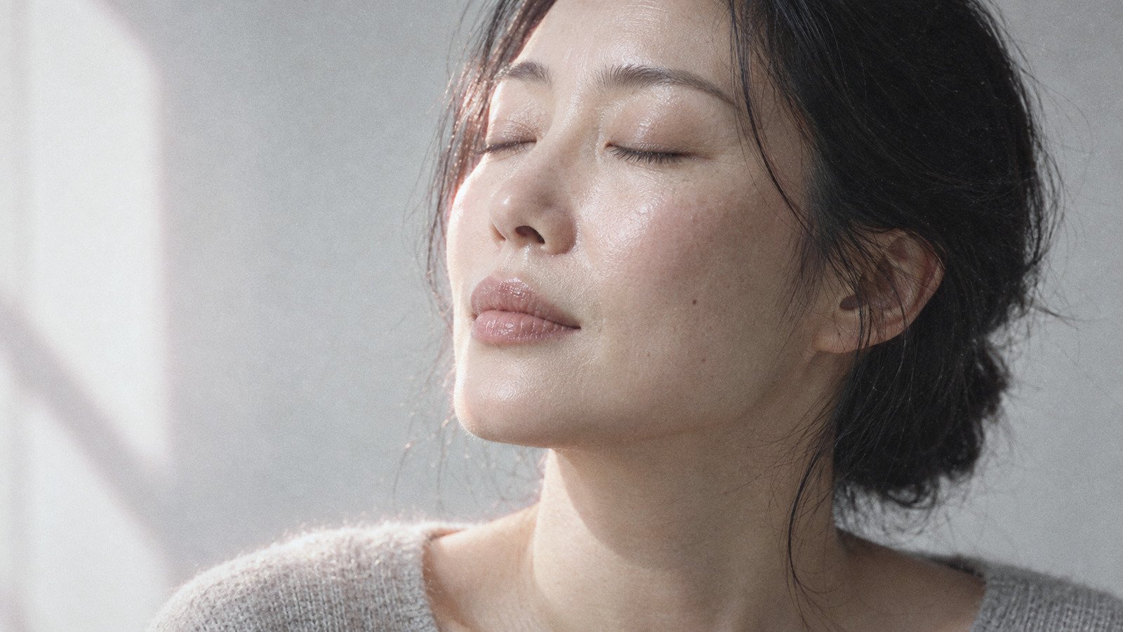 Woman with hydrated natural skin resting her cheek on her hand, eyes closed